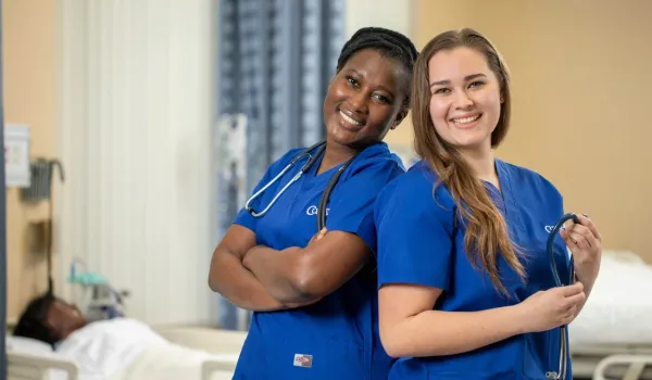 Two Concorde nursing students smiling wearing blue scrubs and stethoscopes