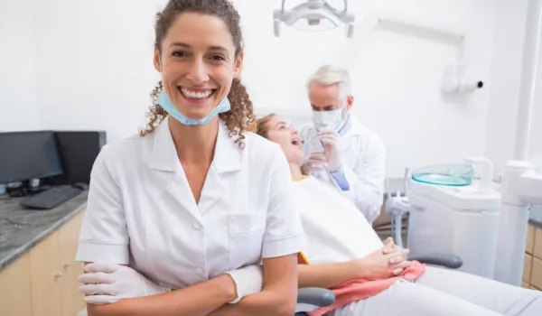 Dental assistant smiling at camera with dentist and patient behind at the dental clinic