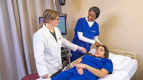 A Neurodiagnostic Technologist attaches probes to patient's forehead as teacher explains procedure..