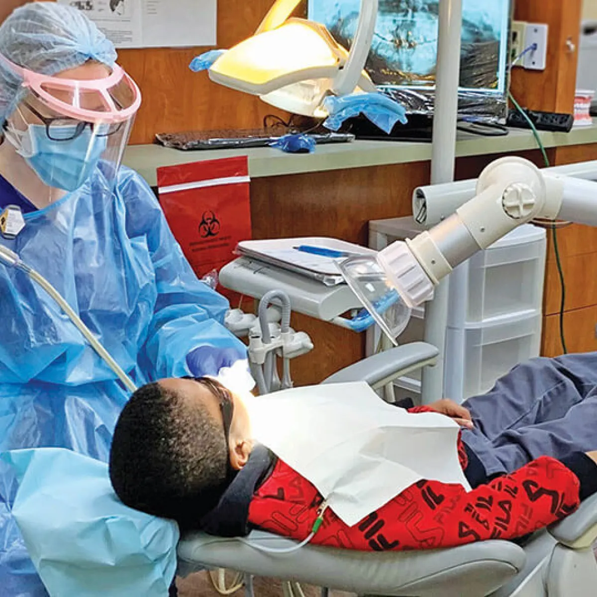 Dental Hygienist in scrubs providing cleaning to young child.