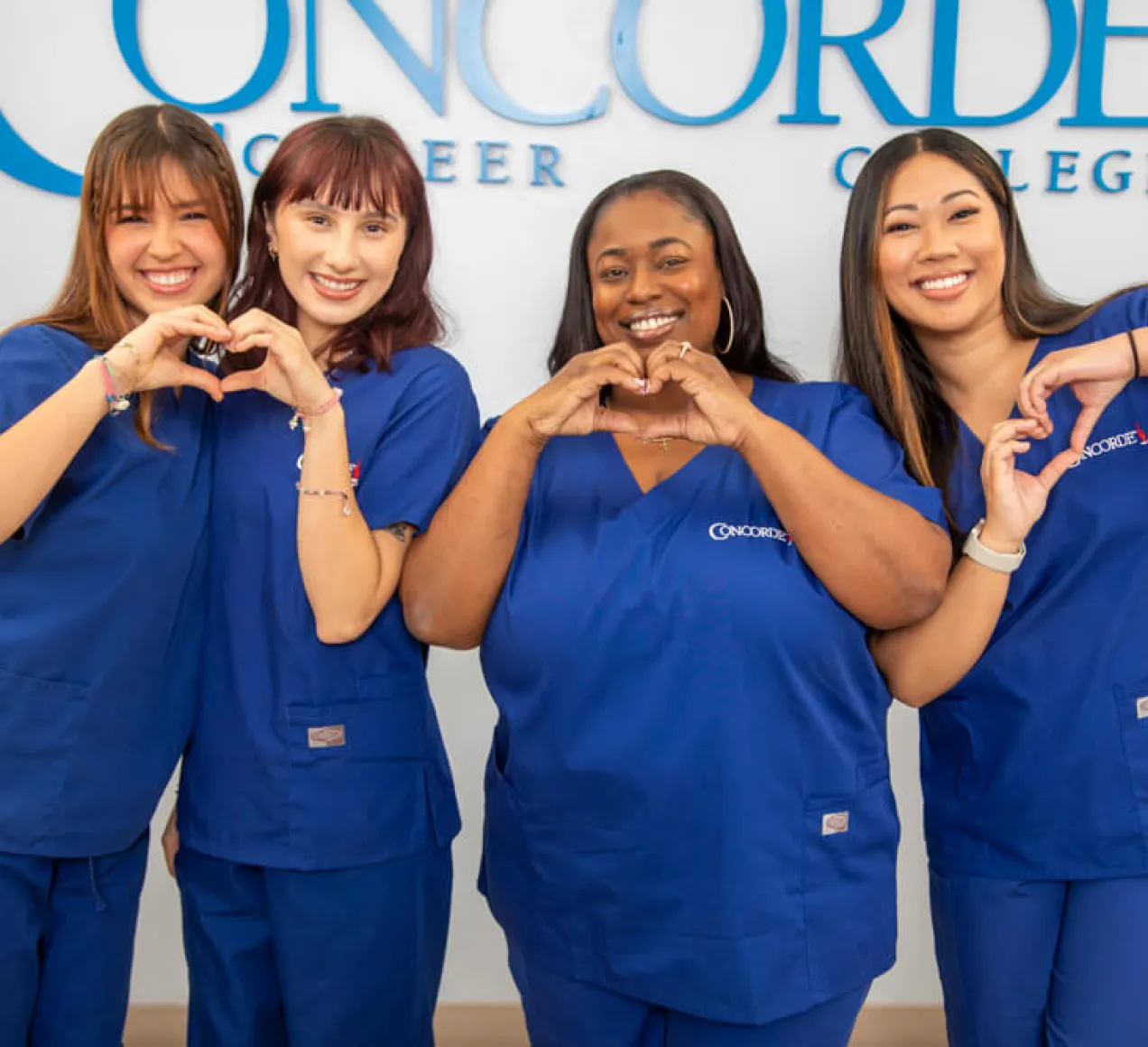 4 smiling Concorde graduates making the shape of a heart with their hands.
