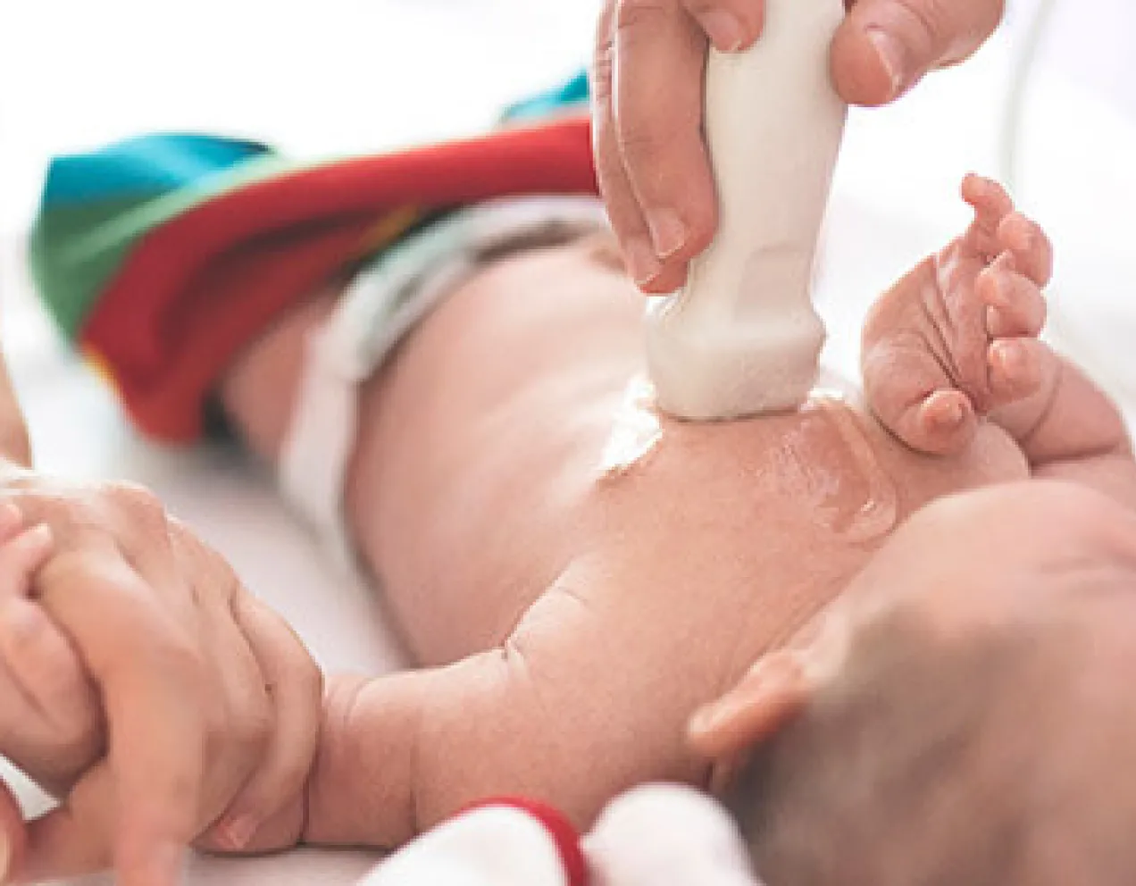 A sonographer performs a cardiovascular sonography on an infant as parent holds baby's hand.
