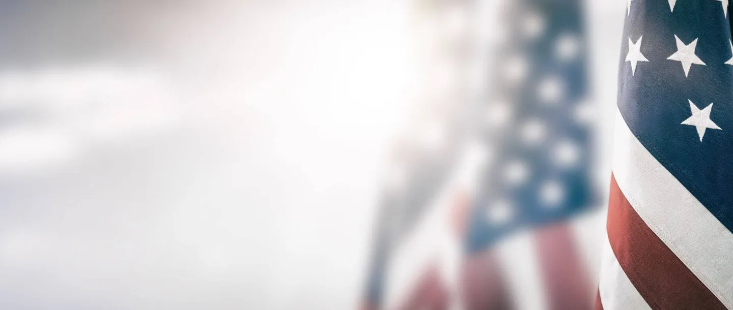 A blurred American flag in the background with bright light, symbolizing the Concorde military tuition support available for veterans and active-duty members.