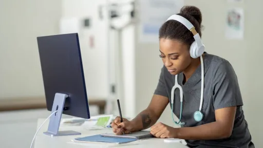 Nursing student with stethoscope taking online RN to BSN classes, studying at a computer with headphones on.