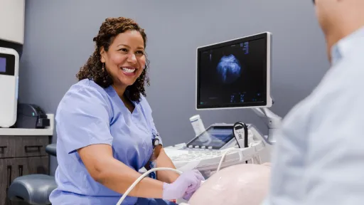 Diagnostic medical sonographer performing ultrasound scan while smiling and interacting with a patient.
