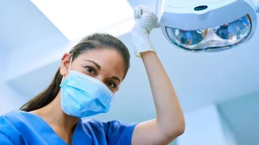 Dental assistant adjusting the overhead exam light, preparing the room for a patient visit as part of daily dental care duties.