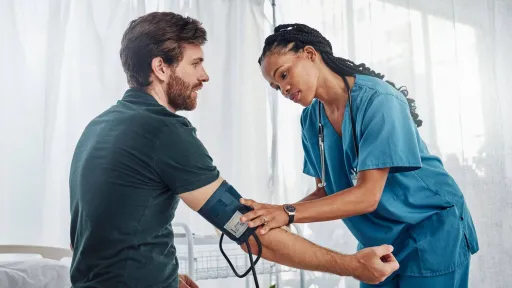 A female medical assistant in blue scrubs using blood pressure cuff on male patient in hospital to take patient vitals medical assistant responsibilities