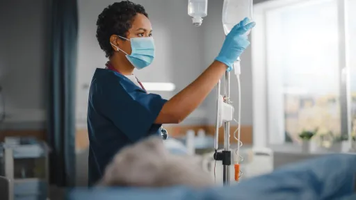 A nursing student in blue scrubs carefully checking and adjusting an IV pump during a clinical training session.