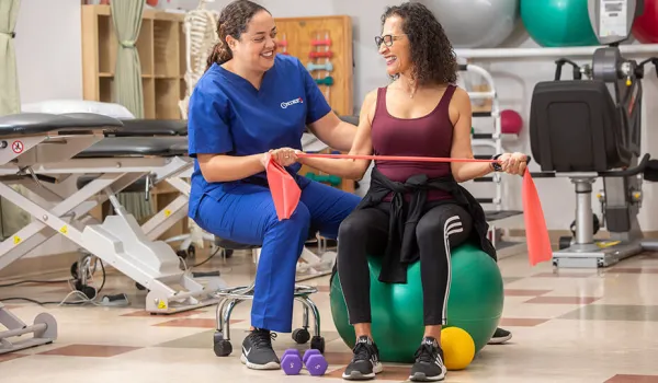 A physical therapist assistant helps her patient with arm band exercise.