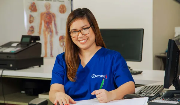 A medical office professional sitting at desk with pen completing paperwork.