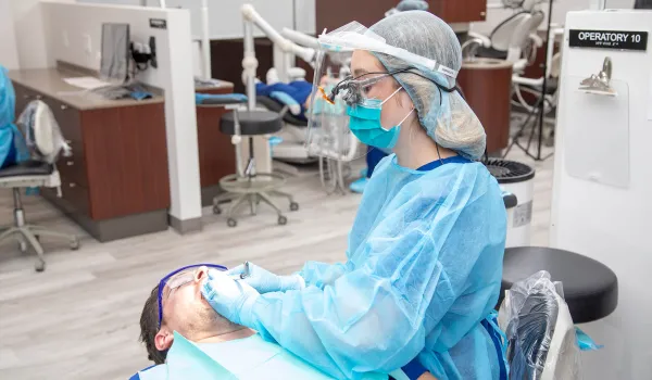 A dental hygienist performs cleaning procedure on male patient.