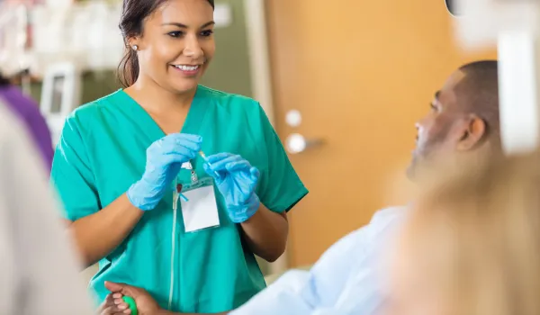 Phlebotomy Technician holding a needle soothes male patient about to give blood.