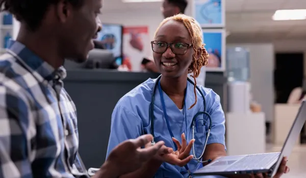 Medical assistant in scrubs discussing intake with patient, representing job duties and clinical work environment.