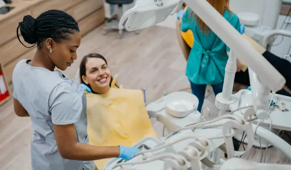 Dental assistant helping a patient in the dental chair during a clinical procedure, reflecting patient care responsibilities in the role.