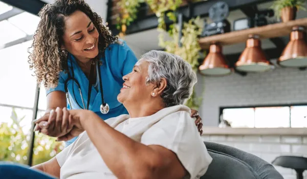 A smiling nurse holds the hand of an elderly patient in a warm, bright room, illustrating the rewarding patient-care aspect of changing your career to nursing.