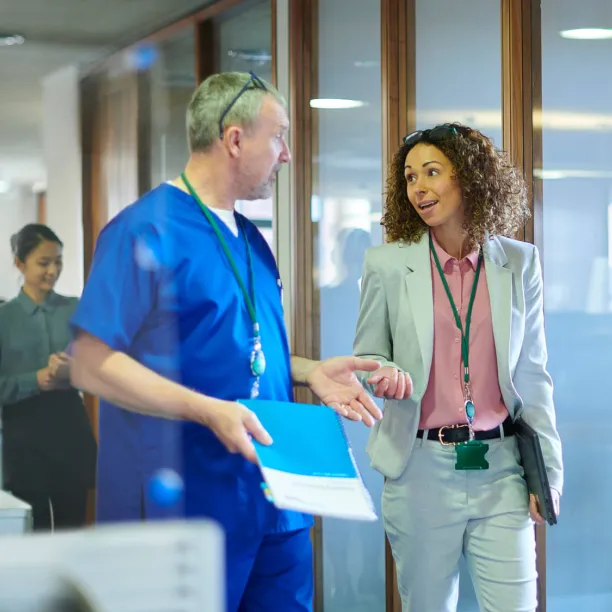 A healthcare administrator speaks with a medical provider as they walk together down the hallway of a medical facility.