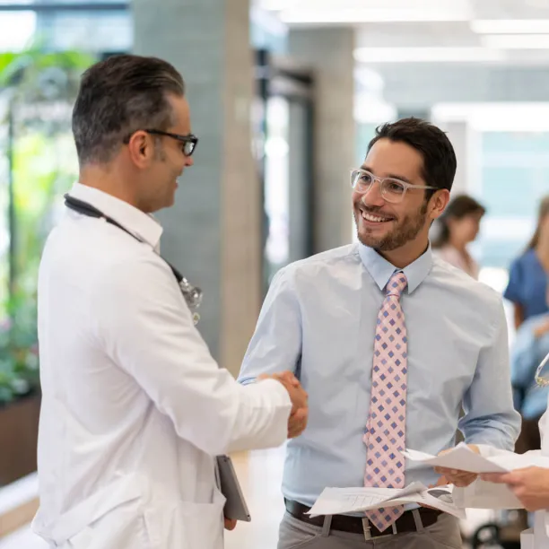 Healthcare Administrator holding papers shakes hands with a doctor in a hospital