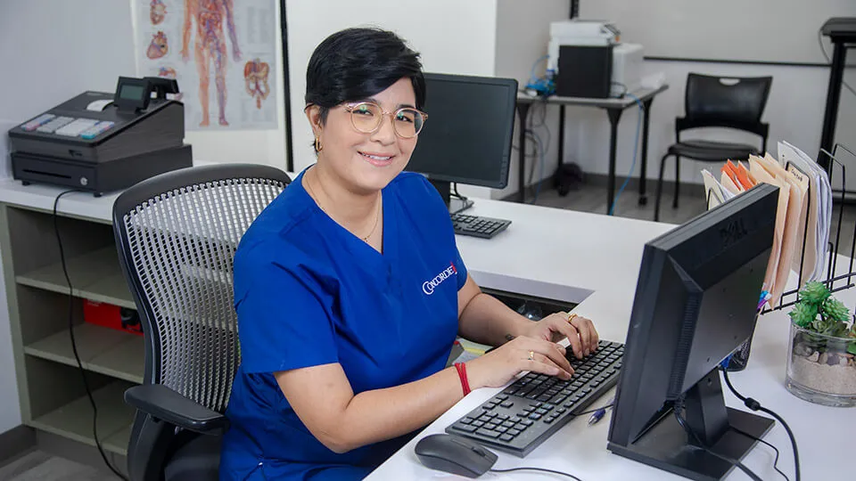 A smiling medical office professional at desk with her hands on keyboard. A smiling medical office professional at desk with her hands on keyboard.