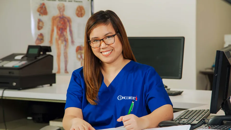 A medical office professional sitting at desk with pen completing paperwork.