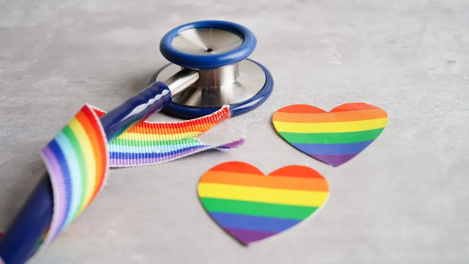 Stethoscope wrapped around rainbow pride ribbon Stethoscope wrapped around rainbow pride ribbon with rainbow pride flag and pride flag hear cutouts on table