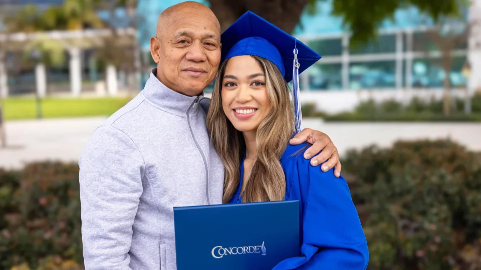 Concorde graduate wearing cap and gown holds degree and poses with proud family member. Concorde graduate wearing cap and gown holds degree and poses with proud family member.
