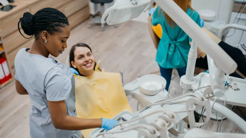 Dental assistant helping a patient in the dental chair during a clinical procedure, reflecting patient care responsibilities in the role.