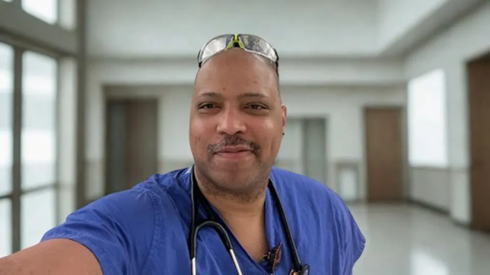 JR in blue scrubs taking a selfie in a hallway