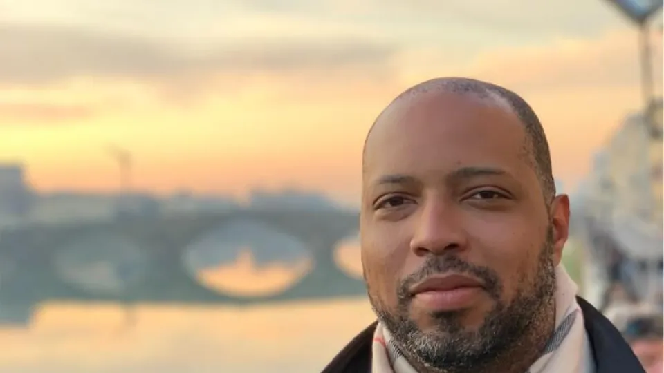 JR in a scarf and nice jacket standing in front of a sunset