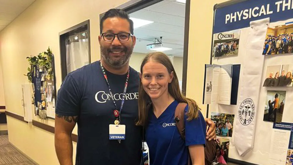 Male-instructor-with-dark-hair-and-glasses-stands-next-to-female-Concorde-physical-therapist-assistant-student-smiling-at-camera
