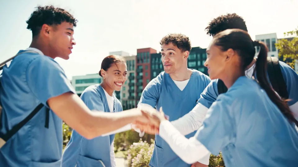 A group of nursing students in scrubs standing together and offering each other encouragement and peer support.