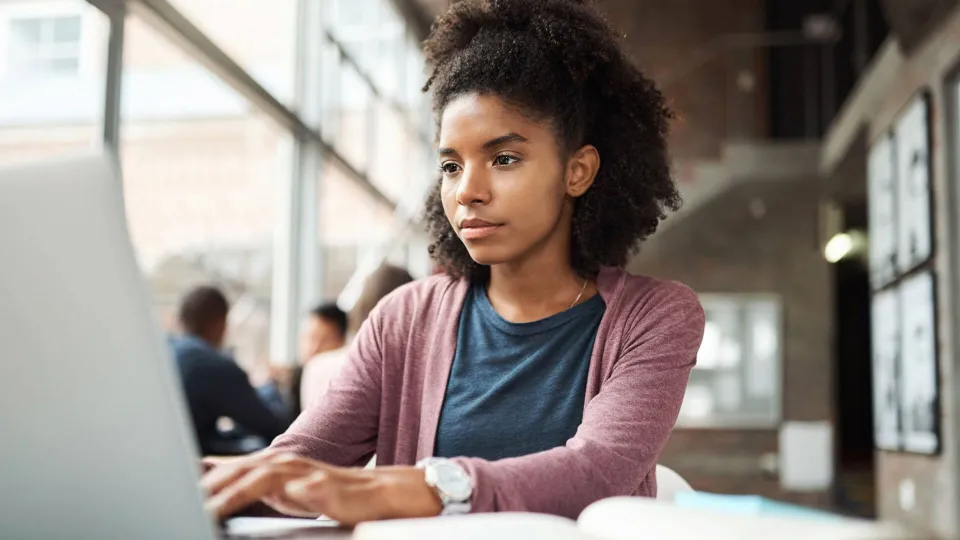 A focused young woman using a laptop in a bright study area to research FAFSA deadlines and submit her financial aid application online.
